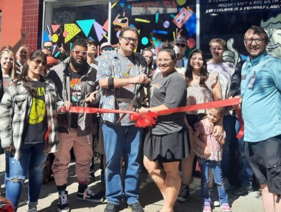 People standing behind a red ribbon holding oversized scissors.
